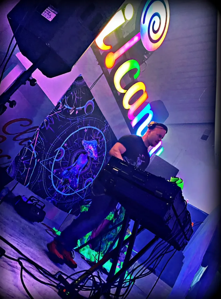 DJ 12K performing on a neon-lit stage under purple lights