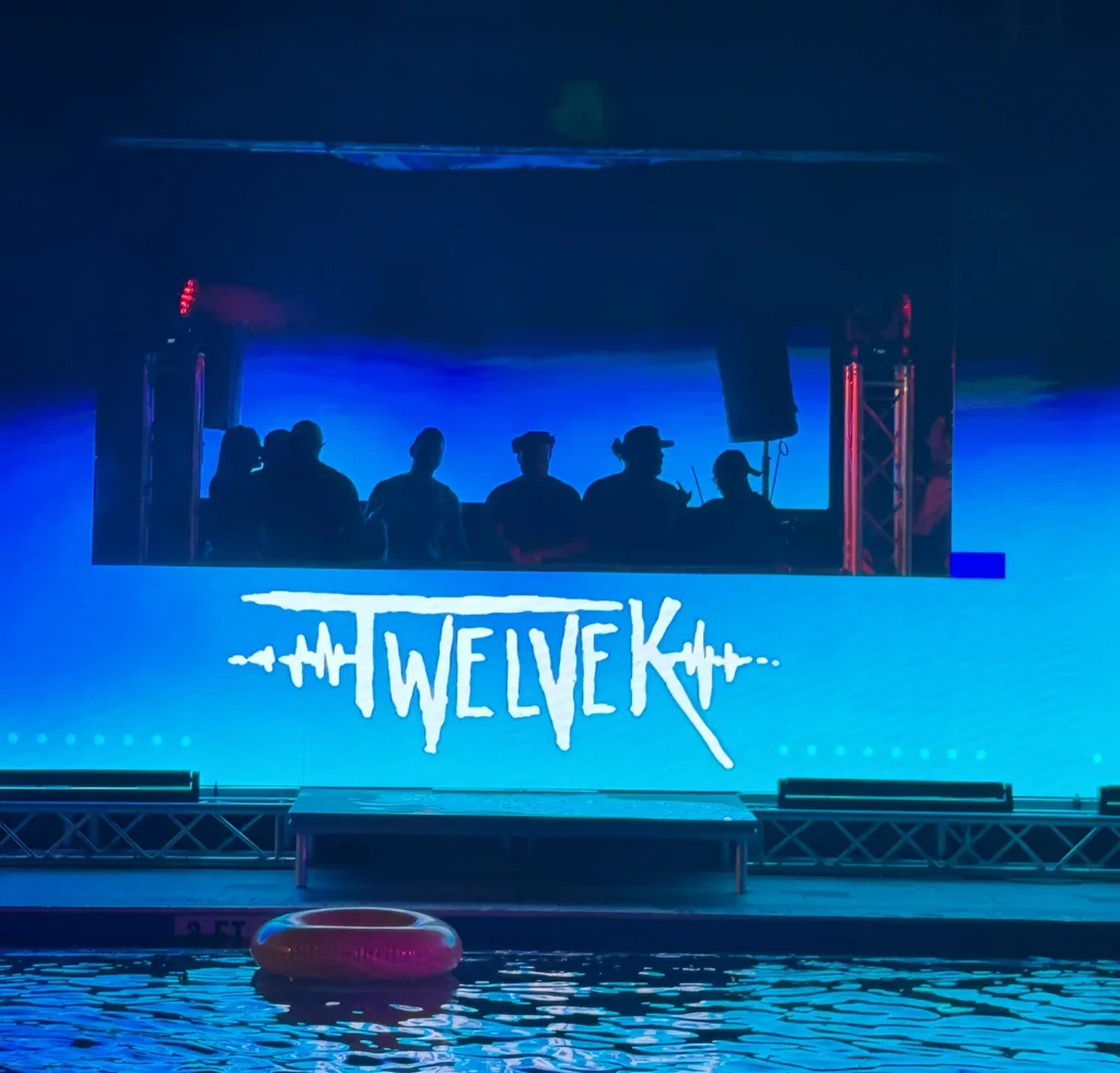 TWELVEK logo on the stage screen above a pool at a night event