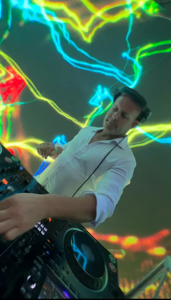 DJ 12K in a white shirt mixing in front of colorful lightning visuals