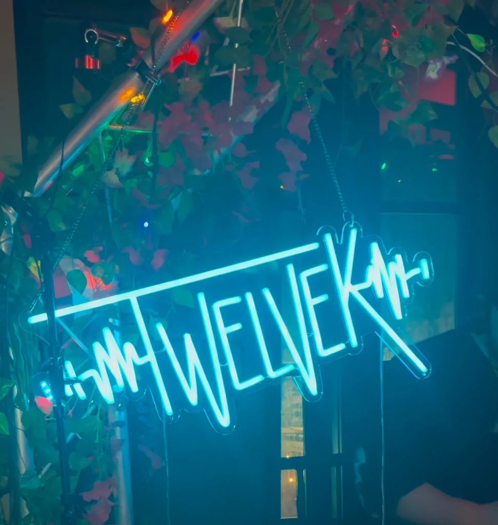 TWELVEK neon sign surrounded by plants