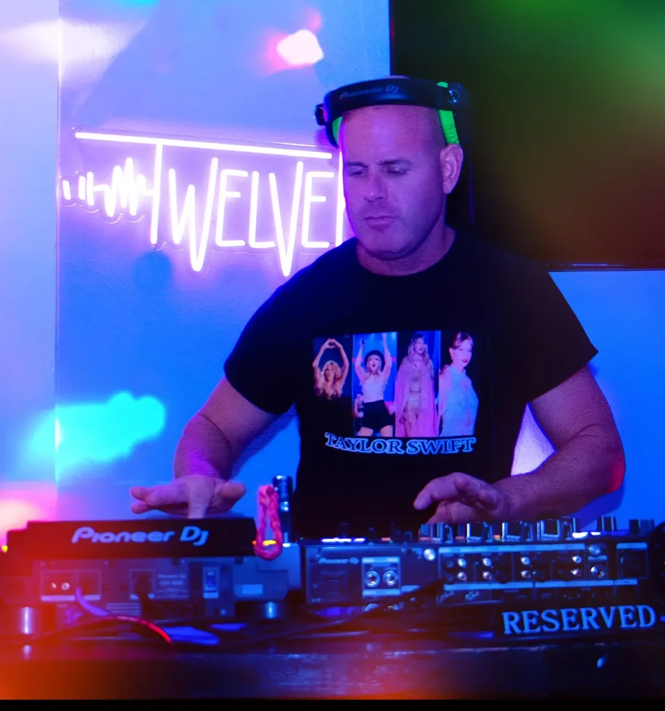 DJ 12K mixing on Pioneer DJ decks in front of a TWELVEK neon sign