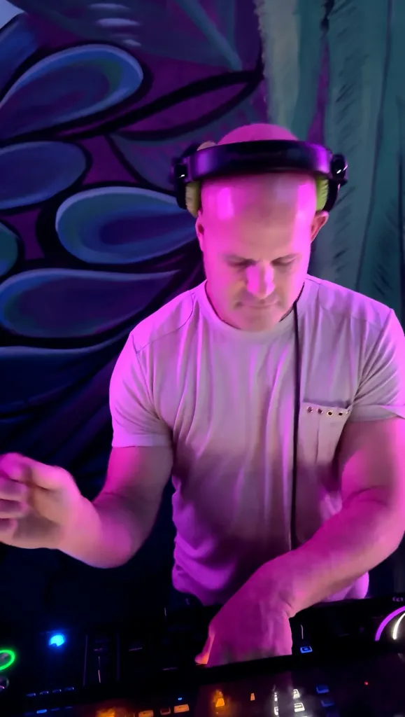 DJ 12K in headphones mixing in front of a purple graffiti mural